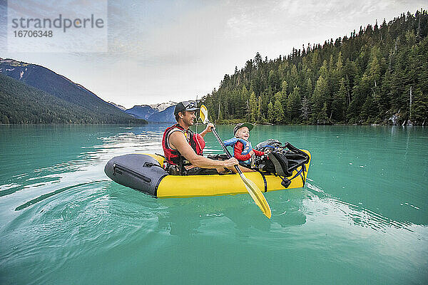 Vater und Sohn lachen  genießen eine Paddeltour auf einem türkisfarbenen See.