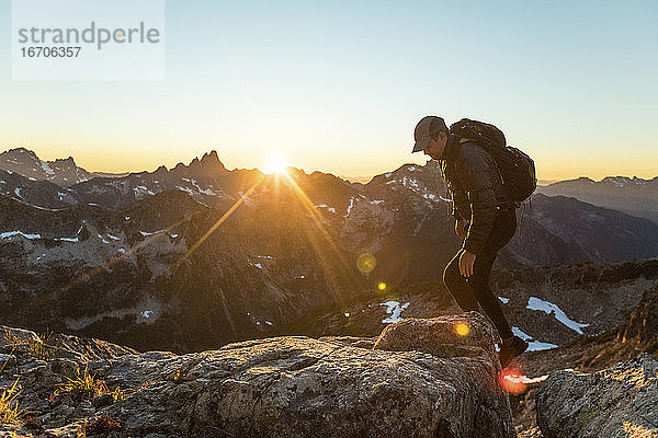 Rucksacktourist  der über felsiges Gelände kraxelt  um den Berggipfel zu erreichen.