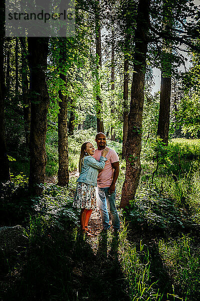Ein gemischtrassiges Paar steht und lacht im Wald