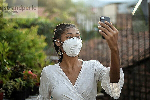 Junge schwarze Frau mit Gesichtsmaske  die ein Smartphone benutzt