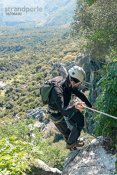Abenteuer. Mann mit Helm  Klettergurt und Rucksack. Abstieg in den Bergen über einen Klettersteig.