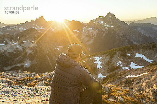 Rückansicht eines aktiven Mannes  der die Aussicht auf die Berge bei Sonnenuntergang genießt.