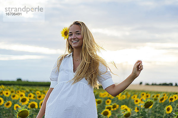 Junge attraktive blonde Frau posiert in ihrem Designerkleid in einem Sonnenblumenfeld