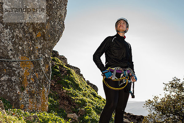 Konzept: Abenteuer. Bergsteigerin mit Helm und Klettergurt. Nachdenklich auf einem Felsen stehend. Blick auf den Gipfel des Berges. Solare Leuchterscheinung. Via ferrata in den Bergen.