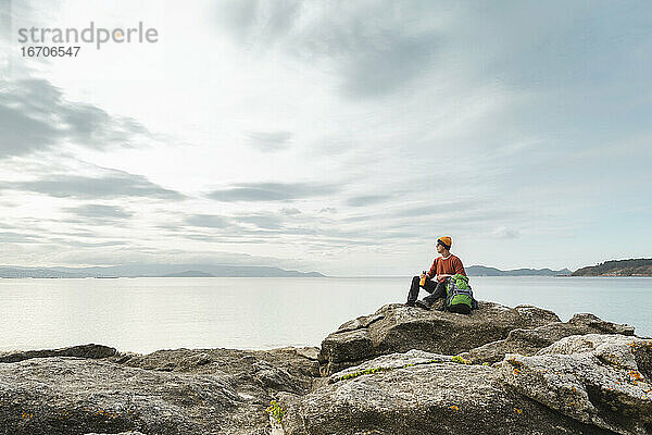 Mann erkundet die Küste auf den Felsen sitzend