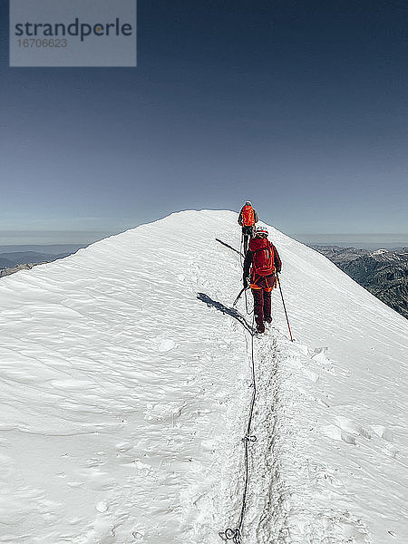 Zwei Bergsteiger beim Aufstieg zum Mont Blanc auf einem Gletscher unter blauem Himmel