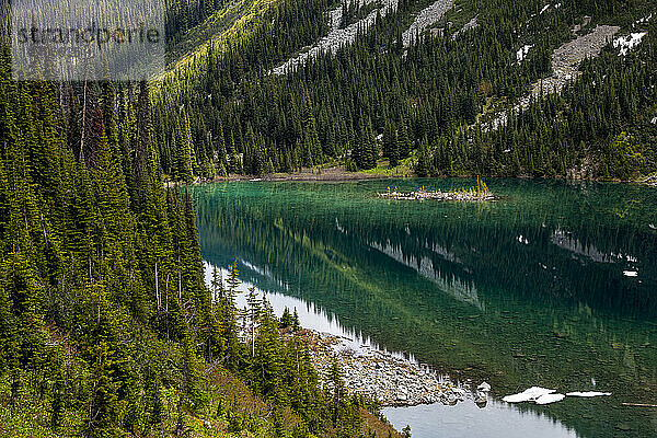 ruhiger See  in dem sich Berghänge mit grünem Wald spiegeln  an einem Sommertag