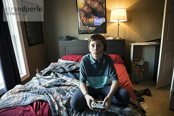 Hohe Ansicht des Teenager-Jungen  der ein Headset trägt und auf dem Bett sitzt