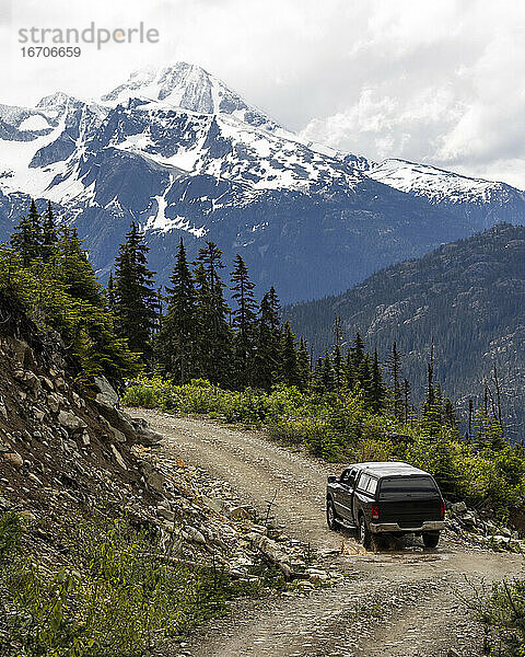 Modernes Fahrzeug auf einer kurvenreichen Forststraße in der Nähe einer rauen Piste während einer Fahrt durch verschneite Berge in British Columbia  Kanada