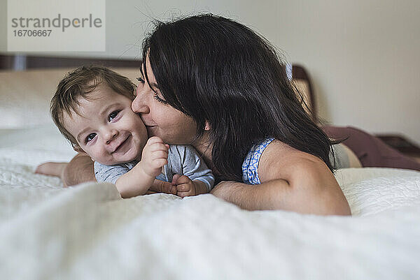 Liebevolle Mutter küsst süßes lächelndes Baby im Liegen auf dem Bett