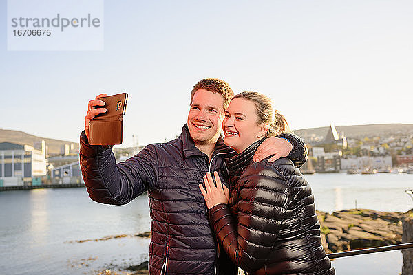 Vergnügtes Touristenpaar macht Selfie an der Strandpromenade