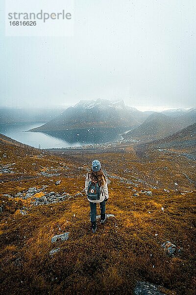 Frau blickt auf den Ort Fjordbotn und einen markanten und spitzen Berg  Schneefall in herbstlicher Fjordlandschaft  Fjordgard  Senja  Norwegen  Europa