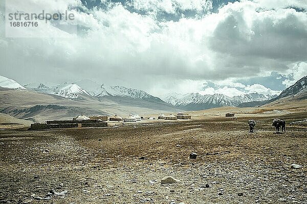 Stallungen aus Stein und Jurten eines kirgischen Nomadenlagers  zwei Männer reiten darauf zu  dahinter die schneebedeckten Gipfel des Hindukusch  Khadz Goz  Wakhan-Korridor  Badachschan  Afghanistan  Asien