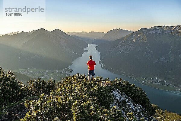 Bergsteiger  junger Mann blickt über Berglandschaft  Latschenkiefern am Gipfel des Bärenkopf  Ausblick auf den Achensee bei Sonnenuntergang  links Seekarspitze und Seebergspitze  Karwendel  Tirol  Österreich  Europa