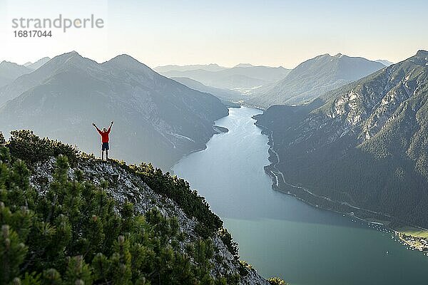 Junger Mann streckt die Arme in die Luft  Blick über Berglandschaft  Ausblick vom Gipfel des Bärenkopf auf den Achensee  links Seekarspitze und Seebergspitze  Karwendel  Tirol  Österreich  Europa