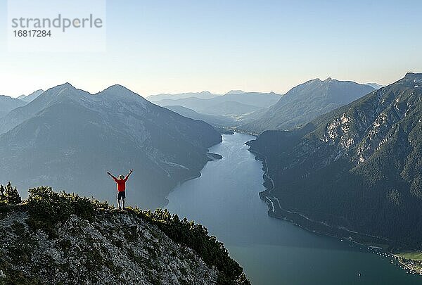 Junger Mann streckt die Arme in die Luft  Blick über Berglandschaft  Ausblick vom Gipfel des Bärenkopf auf den Achensee  links Seekarspitze und Seebergspitze  Karwendel  Tirol  Österreich  Europa