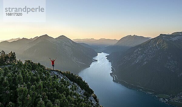 Bergsteiger  junger Mann streckt die Arme in die Luft  Blick über Berglandschaft  Ausblick vom Gipfel des Bärenkopf auf den Achensee  links Seekarspitze und Seebergspitze  Sonnenuntergang in den Bergen  Karwendel  Tirol  Österreich  Europa