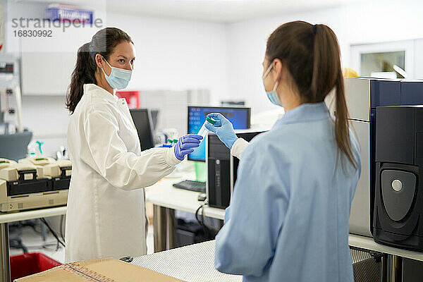 Weibliche Wissenschaftler mit Gesichtsmasken  die eine Probe im Labor halten