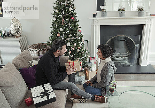 Ehemann gibt Weihnachtsgeschenk an Frau durch Baum im Wohnzimmer