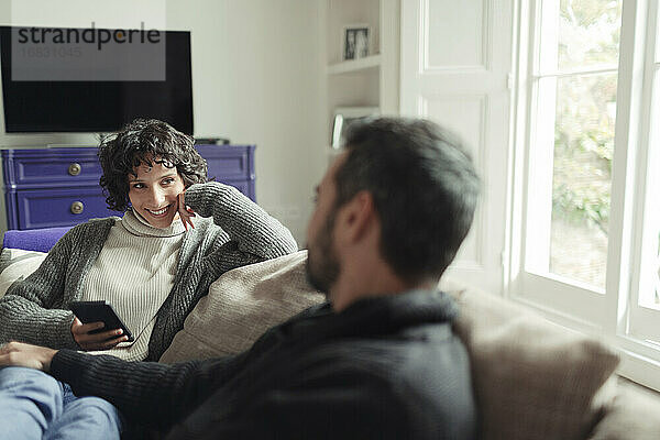 Glückliches Paar mit Smartphone entspannen und reden auf dem Sofa im Wohnzimmer