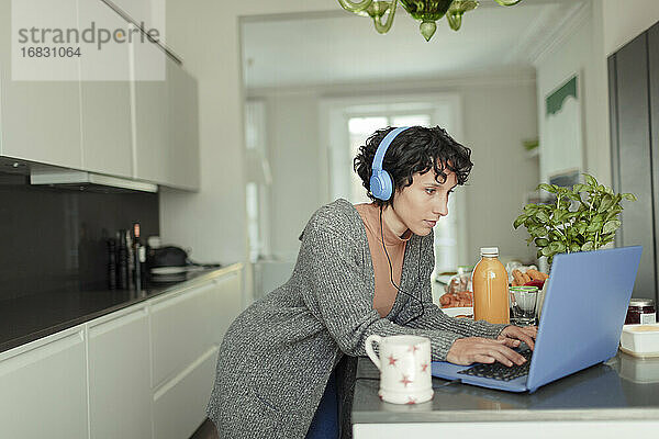Frau mit Kopfhörer arbeiten von zu Hause aus am Laptop in der Küche