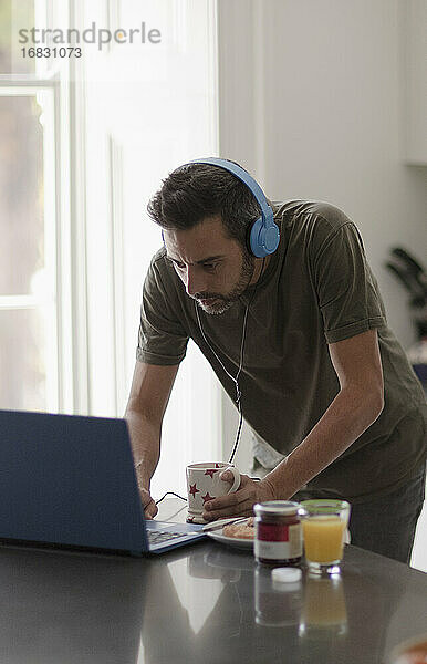 Mann mit Kopfhörer arbeitet von zu Hause aus am Laptop in der Küche