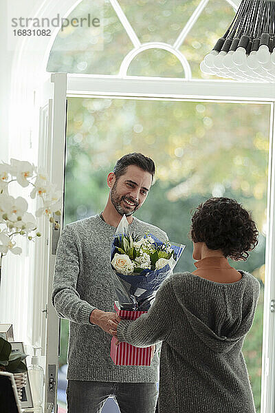 Glücklicher Ehemann überrascht Frau mit Blumen an der Haustür