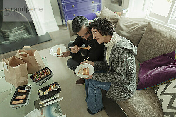 Zärtliches Paar genießt Essen zum Mitnehmen mit Stäbchen auf dem Sofa