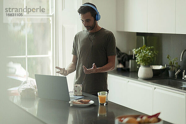 Mann mit Kopfhörern  der von zu Hause aus Videokonferenzen am Laptop abhält