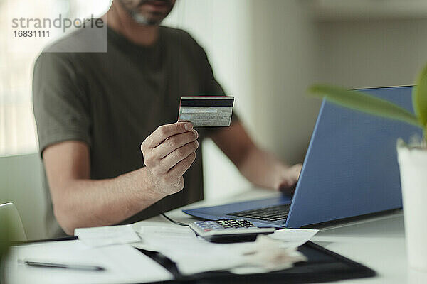 Mann mit Kreditkarte beim Online-Shopping am Laptop