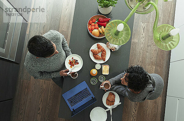 Ehepaar genießt das Frühstück an der Küchentheke mit Laptop