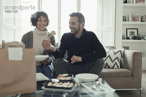 Glückliches Paar isst Essen zum Mitnehmen mit Stäbchen im Wohnzimmer