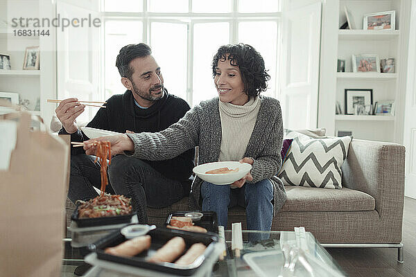 Glückliches Paar genießt Essen zum Mitnehmen mit Stäbchen auf dem Wohnzimmersofa