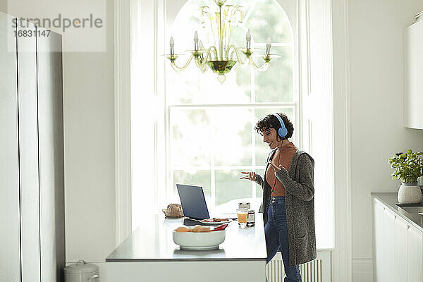 Frau mit Kopfhörer Videokonferenz am Laptop in der Küche