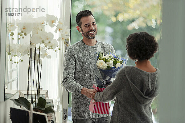Glücklicher Ehemann überrascht Frau mit Blumen an der Haustür