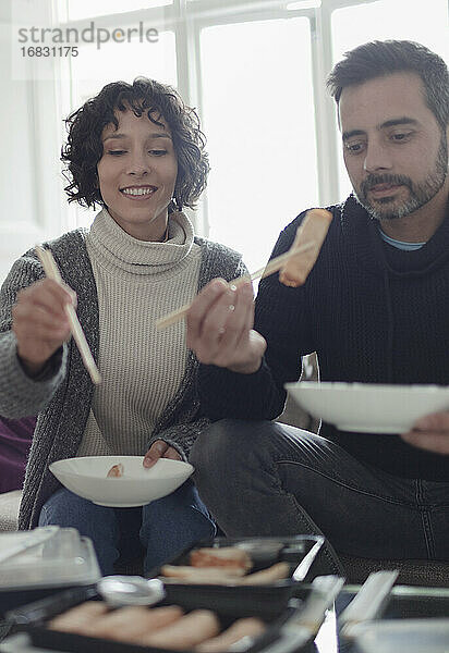 Ehepaar genießt Essen zum Mitnehmen mit Stäbchen im Wohnzimmer