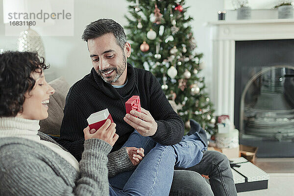 Glückliches Paar öffnet Weihnachtsgeschenk auf dem Sofa im Wohnzimmer