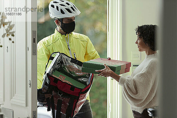 Frau erhält Pizzalieferung von Kurier mit Gesichtsmaske an der Haustür