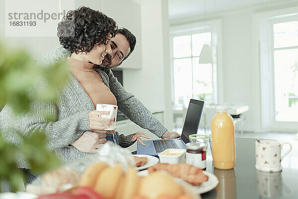 Zärtliches Paar arbeitet am Laptop in der Morgenküche