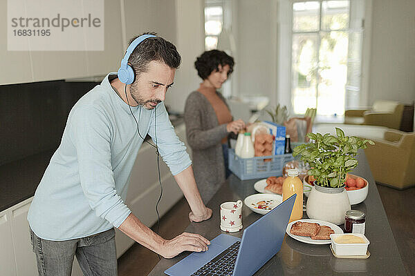 Mann mit Kopfhörer arbeitet von zu Hause aus am Laptop in der Küche