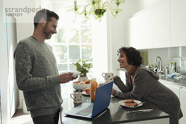 Glückliches Paar genießt das Frühstück und arbeitet am Laptop in der Küche