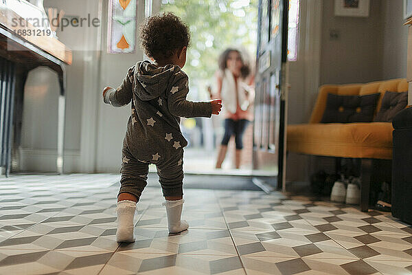 Nettes Baby-Mädchen in Stern-Pyjamas zu Fuß zur Mutter an der offenen Tür