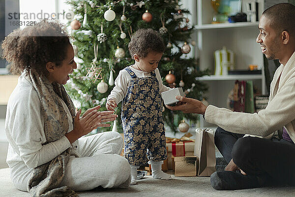 Glückliche Eltern und Baby Tochter Öffnung Weihnachtsgeschenk durch Baum