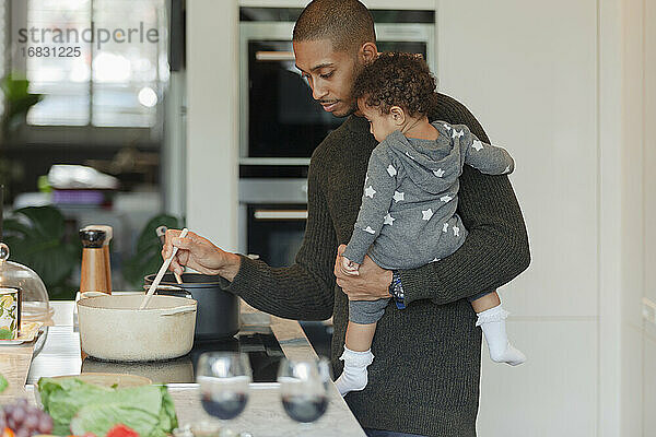 Vater hält Baby Tochter und Kochen Abendessen am Küchenherd