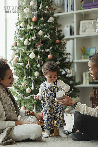 Paar hilft Baby Tochter öffnen Weihnachtsgeschenk im Wohnzimmer