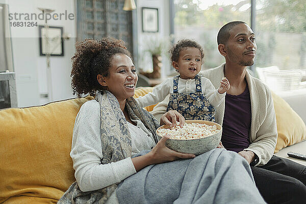 Paar mit Baby Tochter essen Popcorn und Fernsehen auf dem Sofa