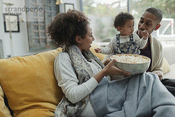 Glückliche Eltern und Baby Tochter vor dem Fernseher mit Popcorn auf dem Sofa