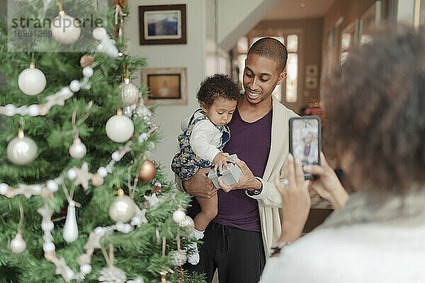 Frau fotografiert Mann und kleine Tochter am Weihnachtsbaum