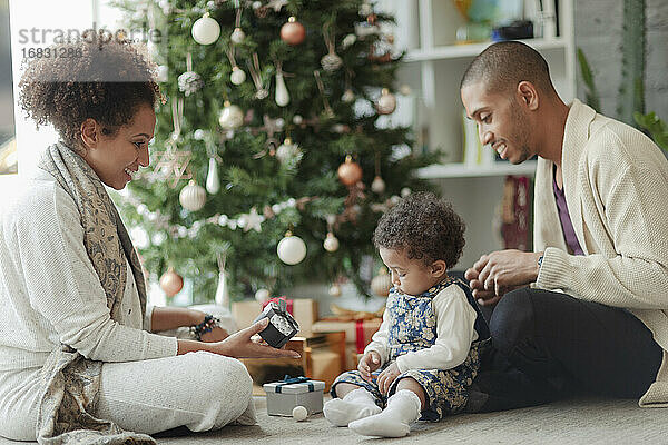 Eltern helfen Baby Tochter öffnen Weihnachtsgeschenke durch Baum