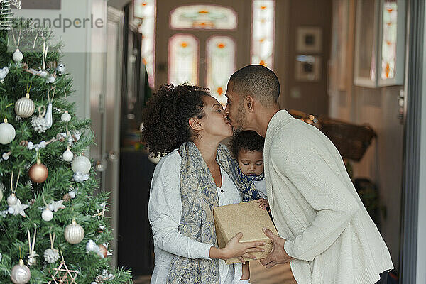 Zärtliches Paar mit Baby Tochter küssen am Weihnachtsbaum